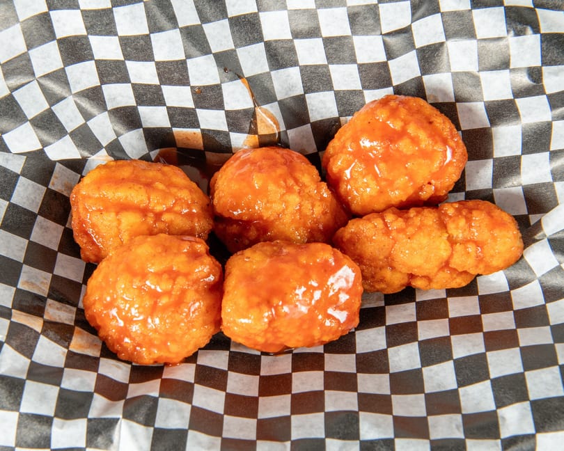 Six orange, saucy boneless wings in a black and white checkered paper-lined basket.