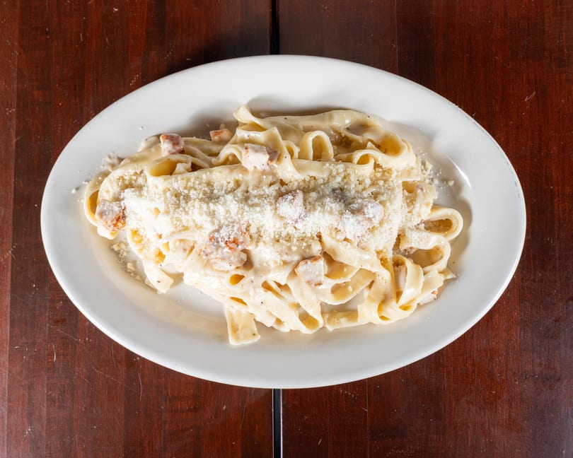 Creamy fettuccine alfredo with chicken and grated Parmesan cheese on a white oval plate.