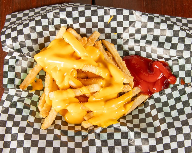 Cheesy fries with a side of ketchup in a black and white checkered paper tray.