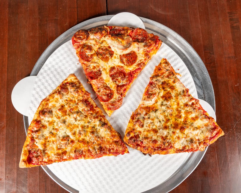 Three slices of pizza, one pepperoni and two sausage, on a metal tray with a white liner.