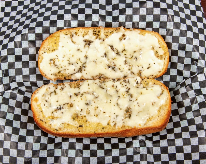 Two halves of cheesy garlic bread with herbs on black and white checkered paper.