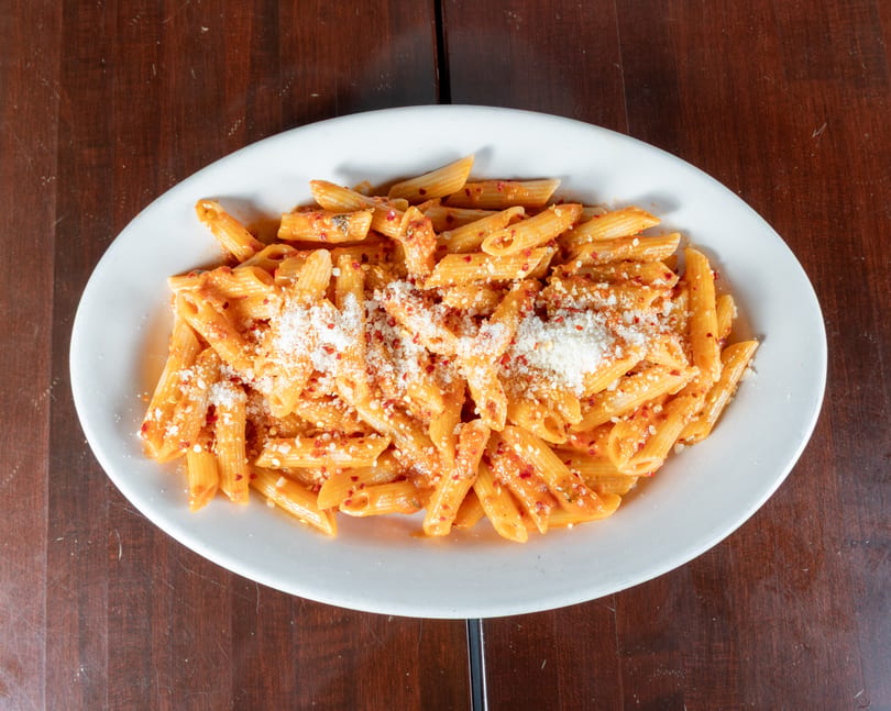 Penne pasta with red sauce, parmesan cheese, and red pepper flakes on a white plate.